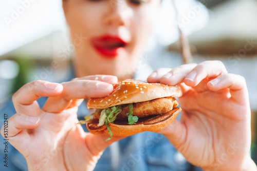 A young glamorous woman with dreadlocks and red lipstick is sitting and eating a burger in a street cafe  the concept of eating. long-lasting lipstick