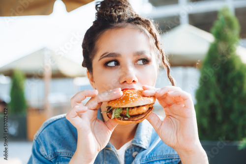 A young glamorous woman with dreadlocks and red lipstick is sitting and eating a burger in a street cafe, the concept of eating. long-lasting lipstick