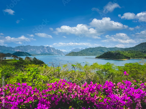 Beautiful lake landscape with flowers and mountain range in background. Bright blue sky, tropical island scene. Amazing natural summer scenery. Travel, tourism, holiday in Khao Sok National Park