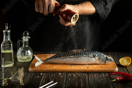 The chef cooks fresh mackerel in the kitchen. Scomber must be added with aromatic pepper before baking