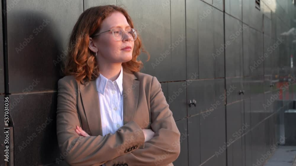 Young businesswoman leaning on building wall with arms crossed Young businesswoman leaning on building wall with arms crossed