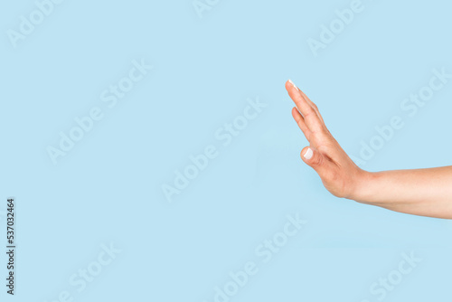 Mano de mujer con la palma abierta haciendo un gesto de stop sobre un fondo celeste liso y aislado. Vista de frente y de cerca. Copy space  photo