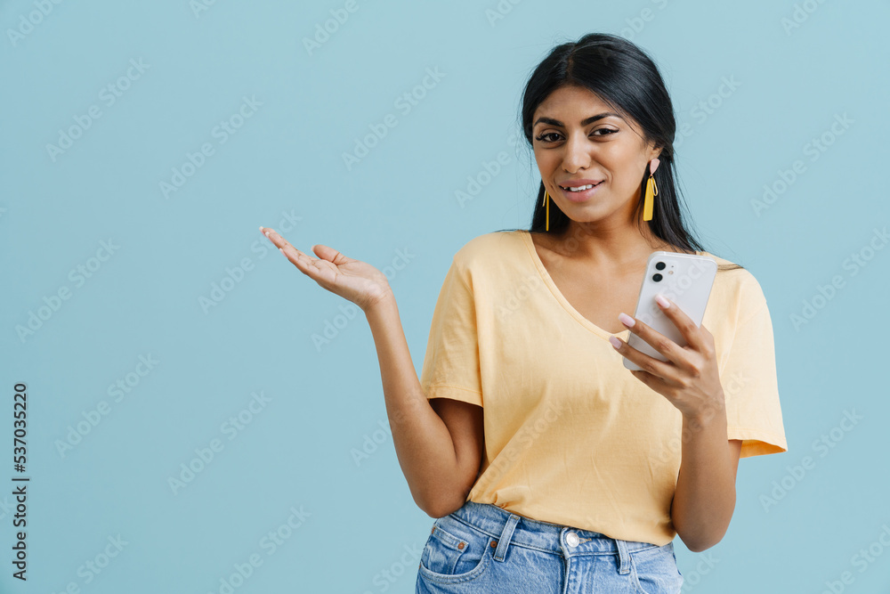 Young indian woman using cellphone while holding copyspace