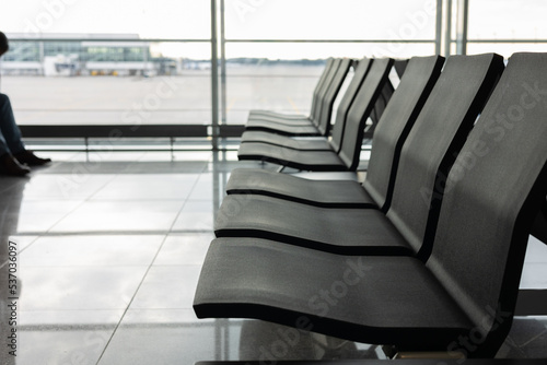 Silhouette shot and selective focus with copy space of waiting chairs or benches in the airport with background of clear window of runway for travelling flight due to vacation and business trip.