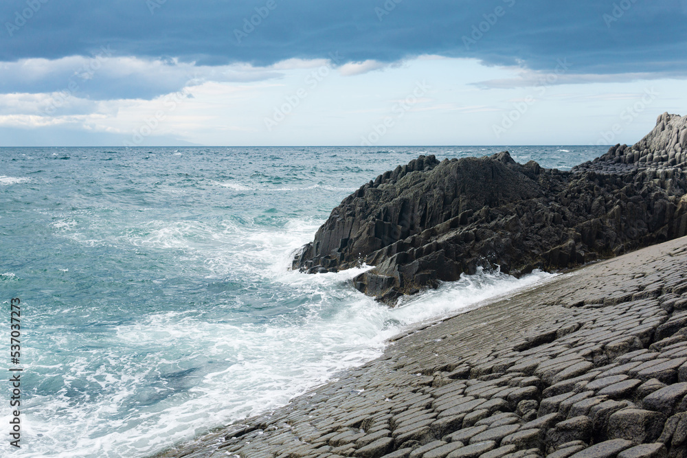 rocky seashore formed by columnar basalt against the surf, coastal landscape of the Kuril Islands