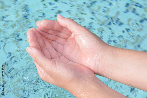 Girl holding water in hands above pool, closeup
