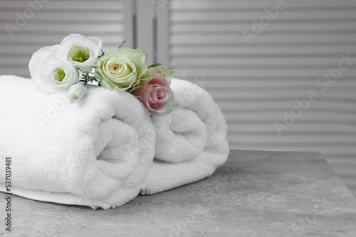 Rolled towels and flowers on grey table indoors, space for text