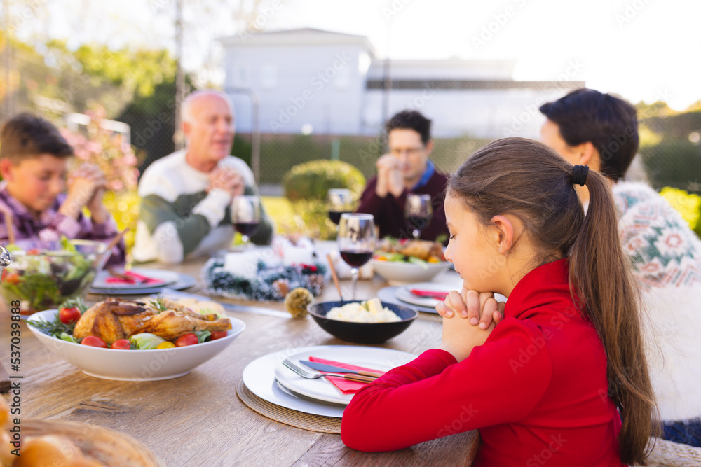 Happy caucasian family spending time together and praying before meal in the garden