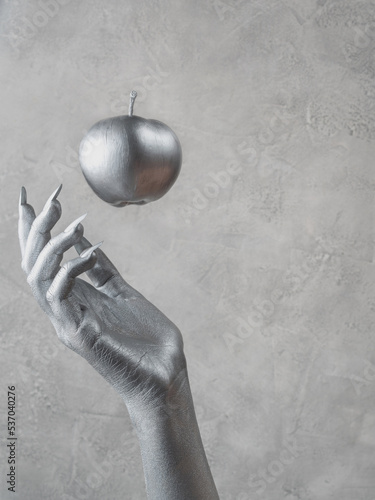 Woman's hand with silver skin catches a silver apple. Close-up, copy space