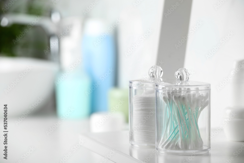 Containers with cotton swabs and pads on white shelf in bathroom. Space for text Containers with cotton swabs and pads on white shelf in bathroom. Space for text