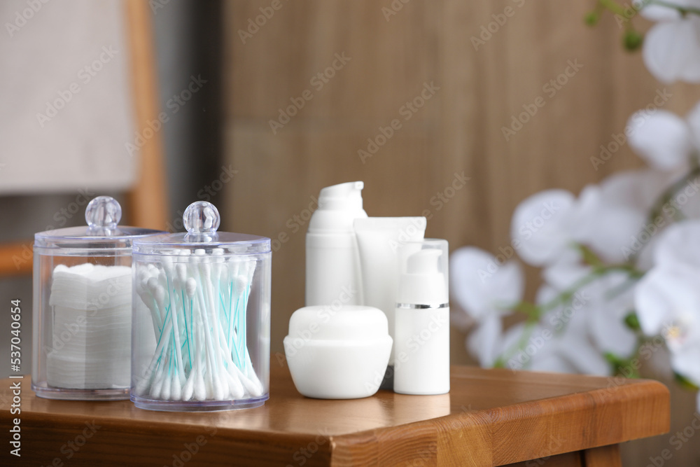 Cotton pads and swabs near cosmetic products on wooden stool in room Cotton pads and swabs near cosmetic products on wooden stool in room
