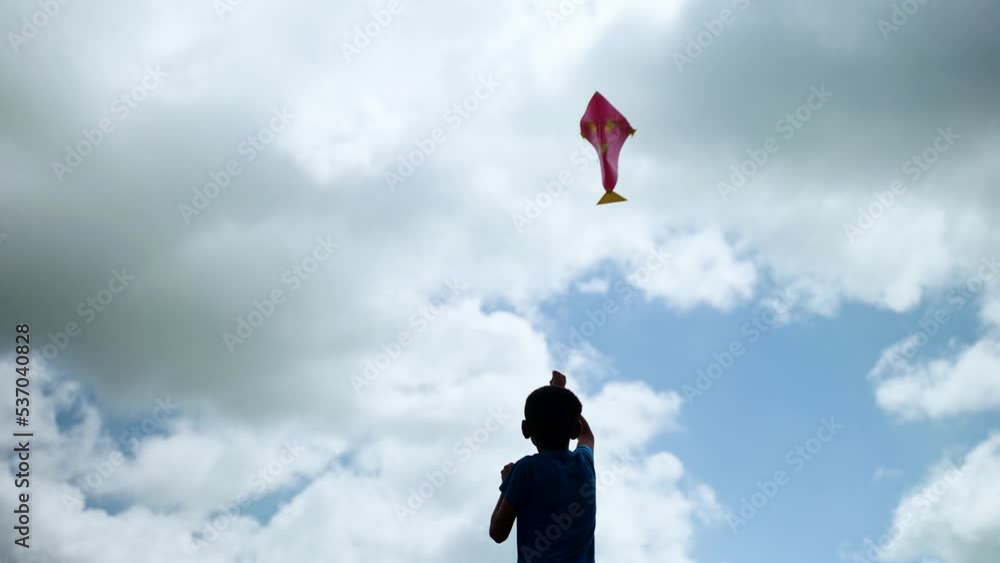 silhouette shot, back view of kid flying kite on blue clouded sky - concept of freedom, development and ambition silhouette shot, back view of kid flying kite on blue clouded sky - concept of freedom, development and ambition