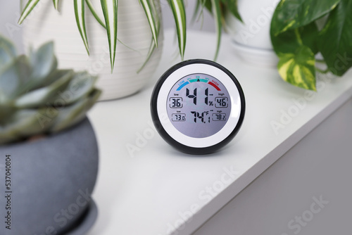 Digital hygrometer with thermometer and plants on white table photo