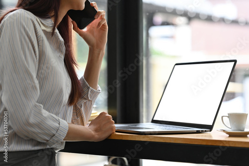 Cropped image of Businesswoman talking on phone while working with laptop, Empty screen of laptop, Business and financial concept.