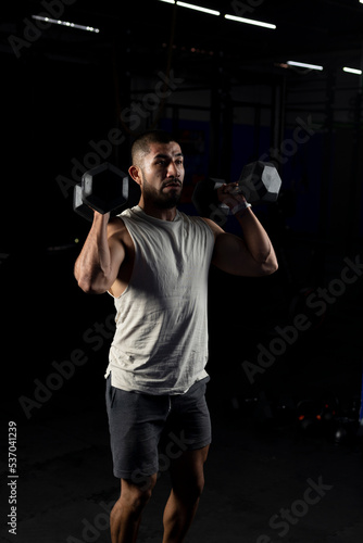 vertical image of a muscular man, pressing with a pair of dumbbells in the gym