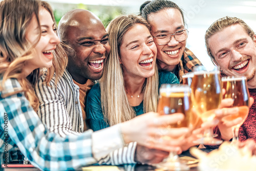Happy friends toasting beer at brewery bar - Multiracial people clinking glasses with brew at house party - Concept about young people having fun together