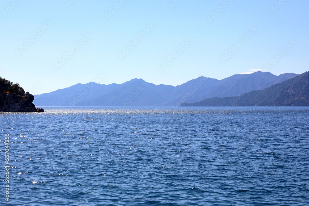 Picturesque view to blue sea and mountain island on horizon in mist. Calm water surface, background for traveling and vacation