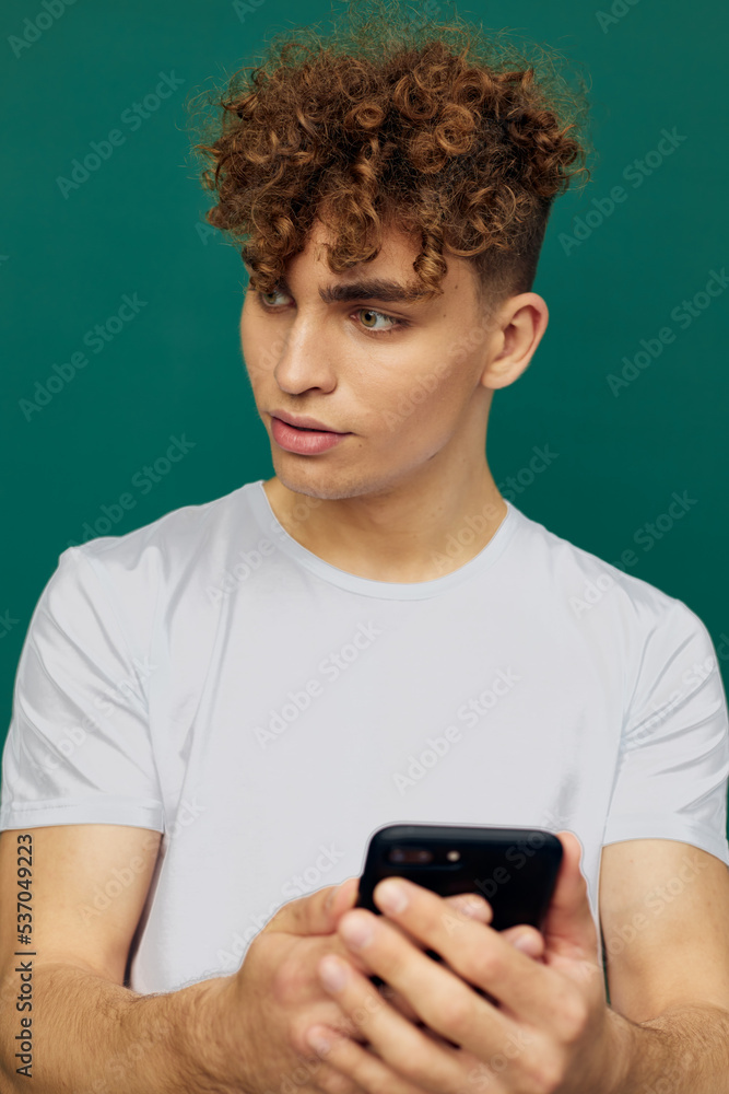 a funny, joyful man with curly hair stands against a green background and holds his smartphone with both hands, looking away with surprise on his face a funny, joyful man with curly hair stands against a green background and holds his smartphone with both hands, looking away with surprise on his face