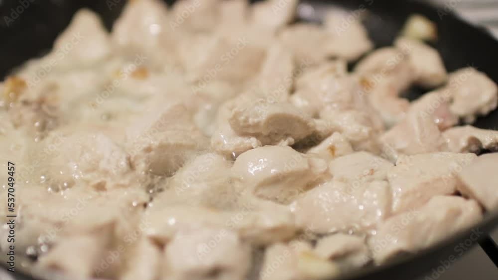 White meat pieces are fried in a black frying pan White meat pieces are fried in a black frying pan