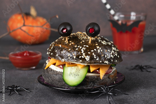 Monster sandwich with black bun, sausage, cheese, cucumber and olive eyes