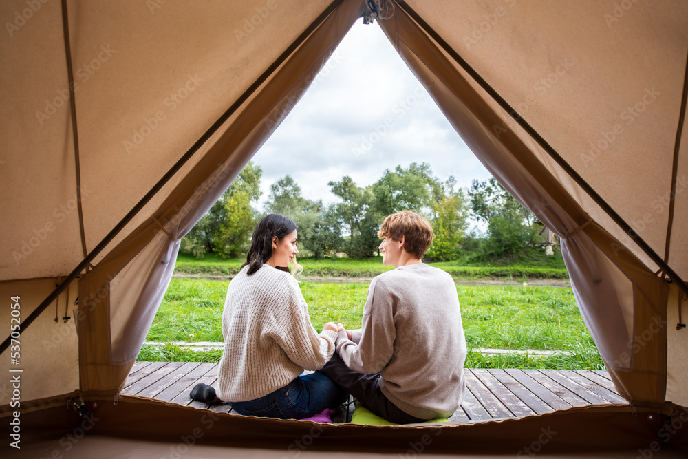 A couple sitting near a tent at glamping A couple sitting near a tent at glamping