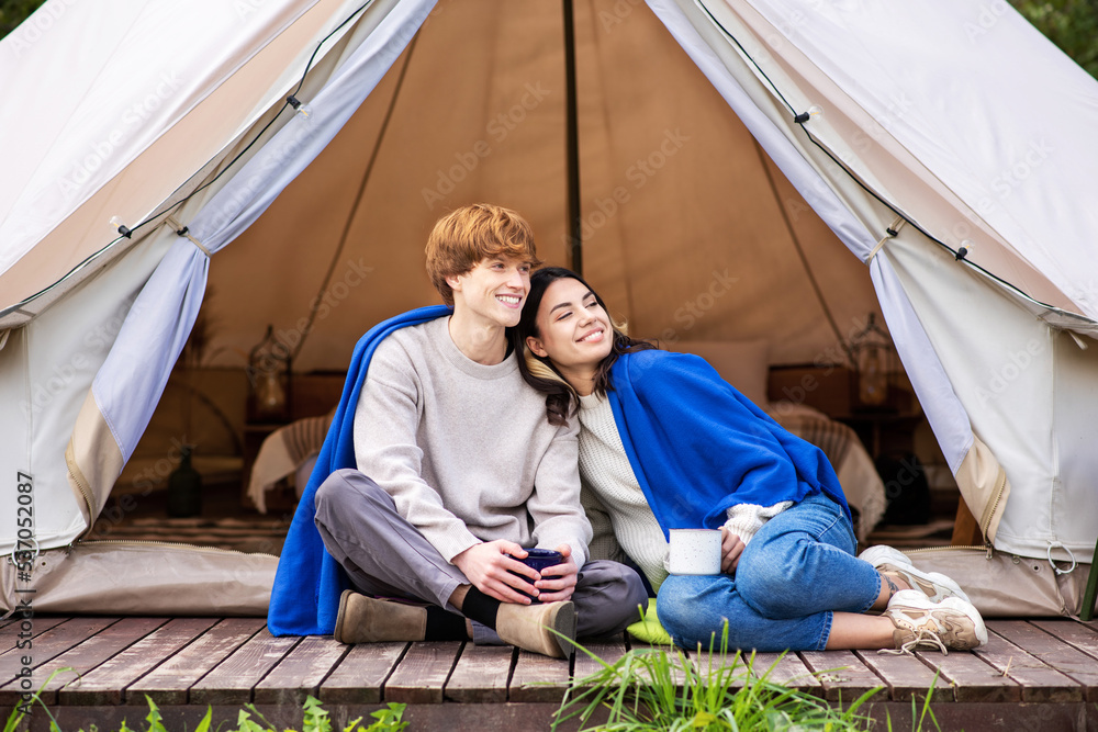 A couple sitting near a tent at glamping A couple sitting near a tent at glamping