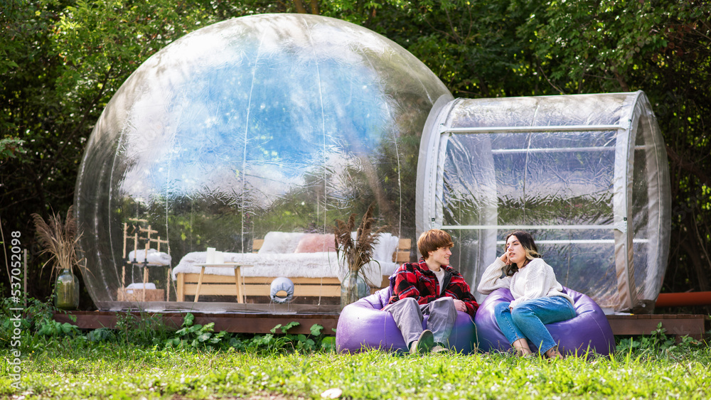 A couple sitting near a transparent bubble tent at glamping