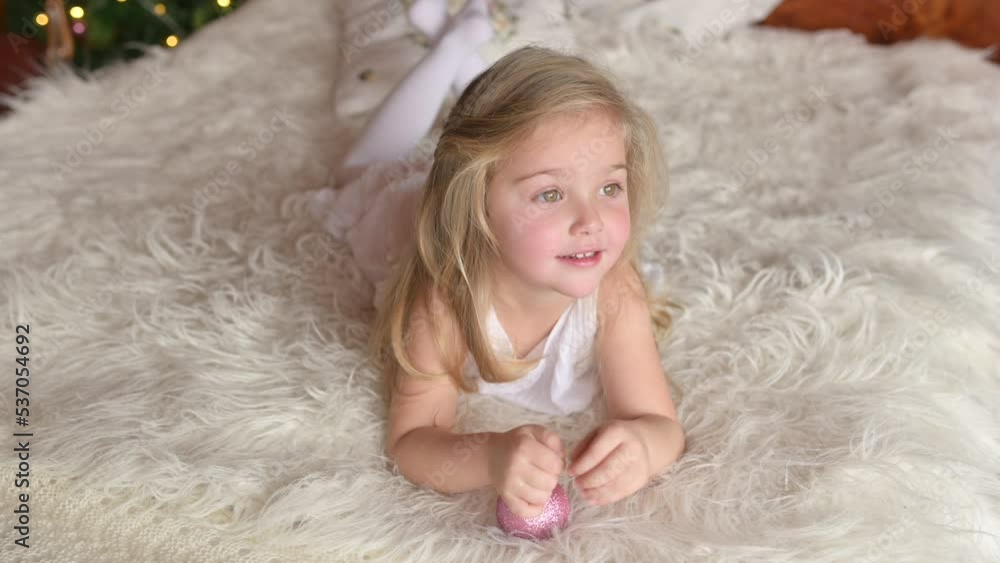 Cute smiling girl lies on the bed holding a Christmas tree decoration, enjoying the festive holiday at home Cute smiling girl lies on the bed holding a Christmas tree decoration, enjoying the festive holiday at home