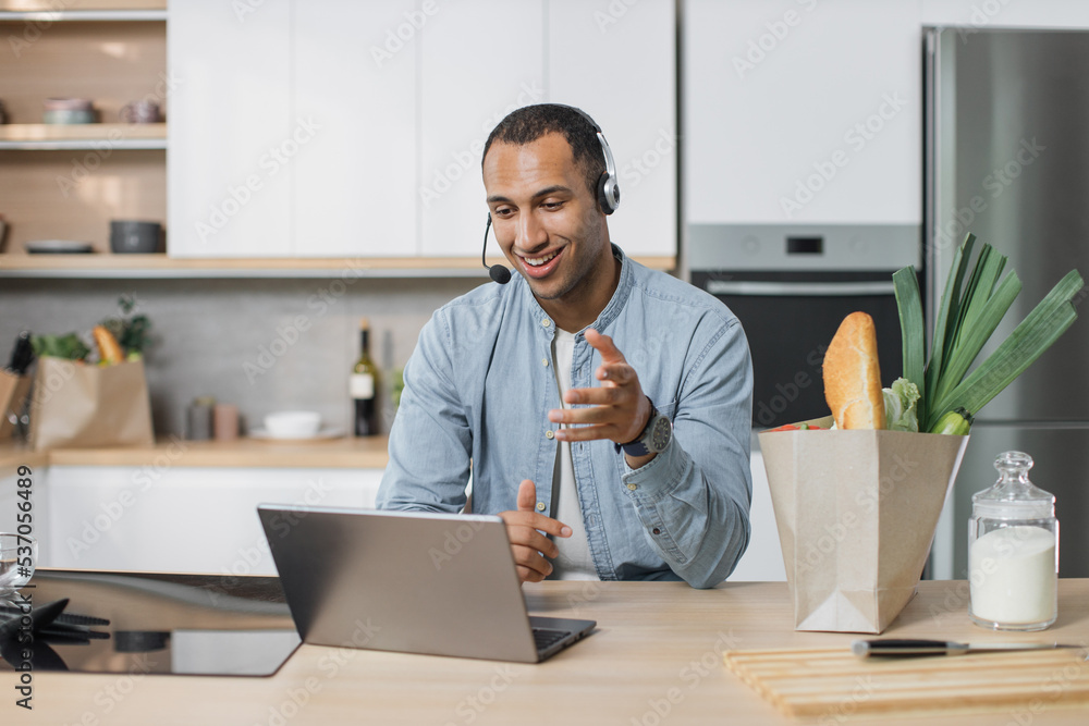 Young arab man, chef sitting in well-equipped modern kitchen having online video conversation with subscribers during vlog session how to cook delicious salad for breakfast looking at laptop . Young arab man, chef sitting in well-equipped modern kitchen having online video conversation with subscribers during vlog session how to cook delicious salad for breakfast looking at laptop .