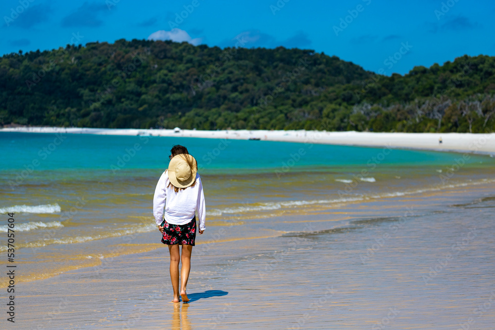 beautiful girl in dress and shirt and hat walks on paradise beach with white sand and turquoise water; walk on whitehaven beach on whitsunday island in queensland; paradise beaches of australia; sunny