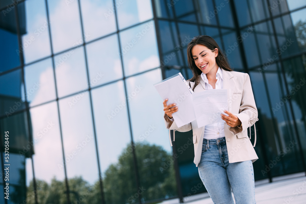 Happy and successful business woman with documents outside office smiling in business suit Happy and successful business woman with documents outside office smiling in business suit