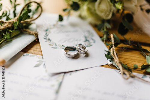 Stylish rings, flowers on wooden table background. Letters from the bride and groom. Vows. Engagement. Luxury marriage and wedding accessory concept. photo