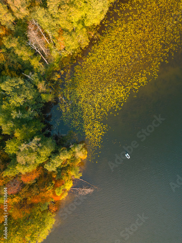 Autumn. A small boat with a fisherman on the lake. View from above.