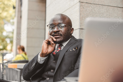 Portrait of black african american businessman in suits sits at a table in a summer cafe with a laptop outdoors