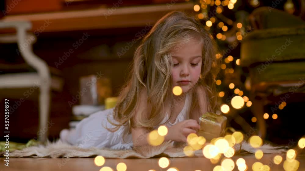 christmas spirit. Happy Cute Little Girl opens a Christmas present while lies on the floor against the background of a festive Christmas tree. Merry Christmas and Happy new year. Happiness. christmas spirit. Happy Cute Little Girl opens a Christmas present while lies on the floor against the background of a festive Christmas tree. Merry Christmas and Happy new year. Happiness.