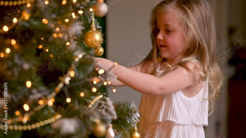 Happy little girl decorating christmas tree with balls. Lots of gift boxes under the tree. children decorating a Christmas tree.	