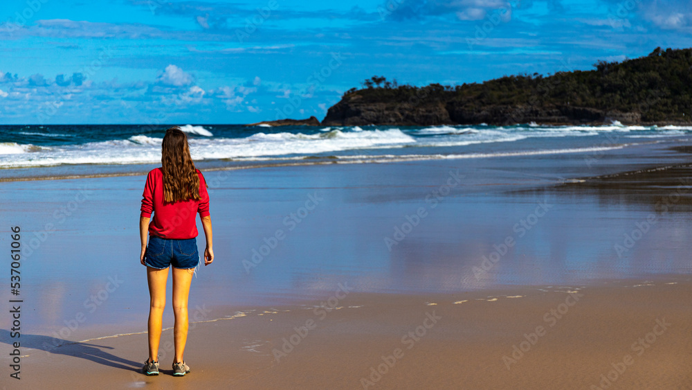 long-haired girl stands on the ocean shore in noosa national park, australia, with big waves in front of her; vacation in queensland, australia, 