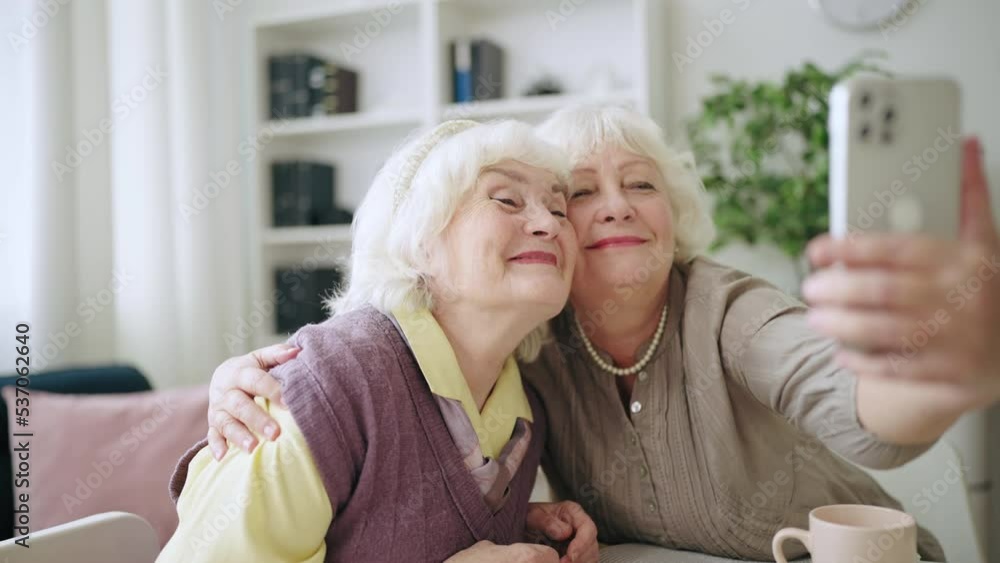Smiling elderly sisters taking selfie using smartphone, contemporary grandmas Smiling elderly sisters taking selfie using smartphone, contemporary grandmas
