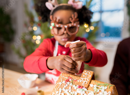 Girl decorating gingerbread house. Kids assembling  tasting gingerbread cookies for Christmas holidays. Happy moments at home concept