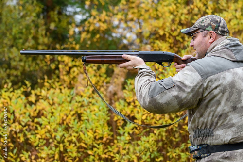 The hunter aims at the target - prey from a hunting gun in the forest in a light autumn rain. A hunter with a gun in his hands at the opening of the hunting season.Shooting with weapons on the hunt.