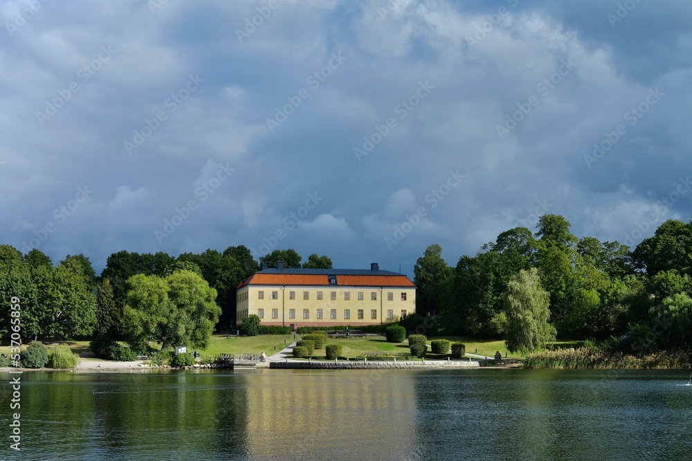 Swedish castle is located in a beautiful park facing the waterfront. Dark clouds hang over an old mansion.