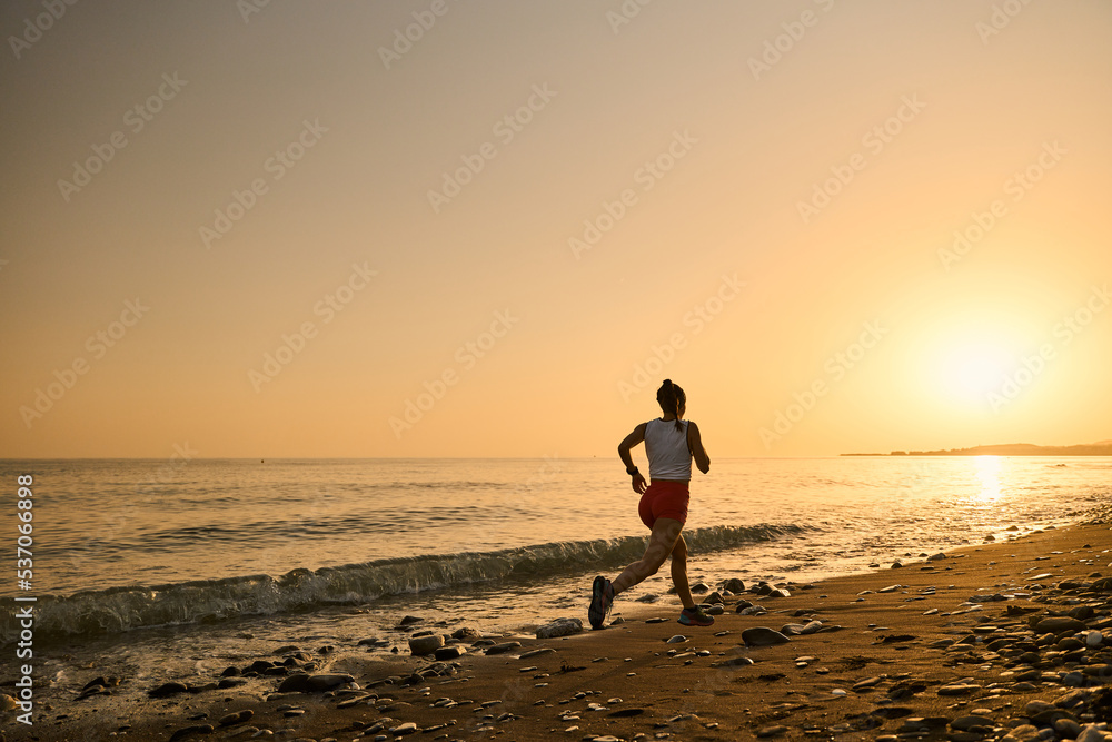 young woman enjoying a run in a pebbly beach at the sunset