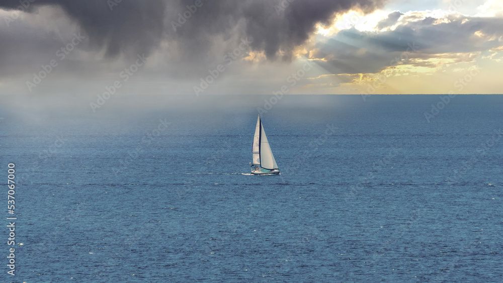 A sailboat gets to safety from an approaching storm at sea