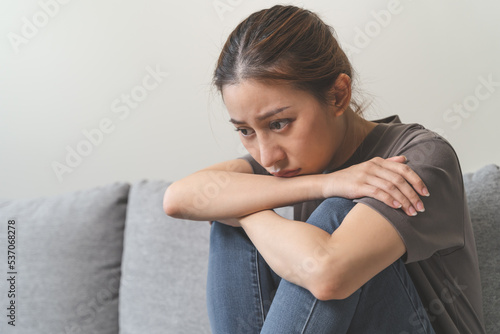 Unhappy anxiety young Asian woman covering her face with pillow on the cough in the living room at home.