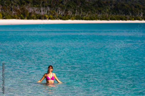 A beautiful girl in a bikini enjoys a dip in the turquoise water on whitehaven beach; relaxing on paradise beaches on whitsunday islands, queensland, australia