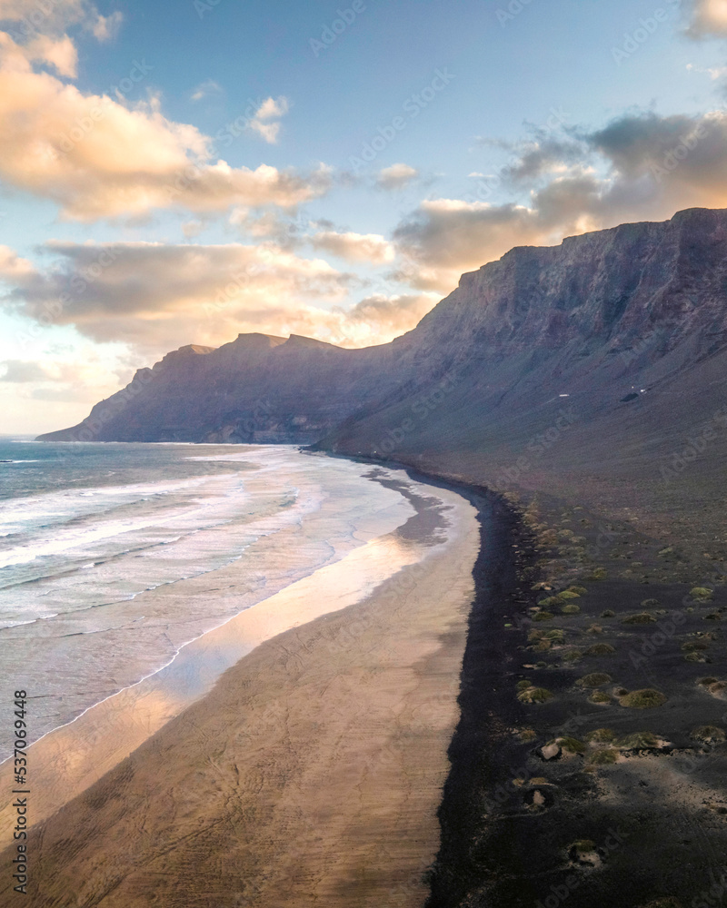 Aerial view of the wild coastline at sunrise along the coast in Caleta de Famara, a famous surf destination in Lanzarote, Canary Islands, Spain. Aerial view of the wild coastline at sunrise along the coast in Caleta de Famara, a famous surf destination in Lanzarote, Canary Islands, Spain.