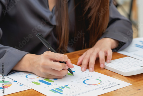 Businesswoman using pen and calculator to calculate customer balance through graph document at office desk