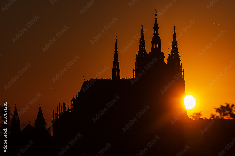 Sunrise behind Prague Castle which is silhouetted against the light orange sky.