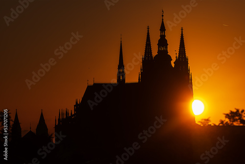 Sunrise behind Prague Castle which is silhouetted against the light orange sky.