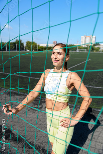Women and sport. Beautiful girl in summer sportswear stands behind the sports net and smiles on the green grass of a stadium. Middle aged sportswoman © borislav15